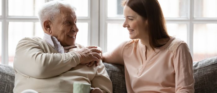 Happy smiling elderly father enjoy conversation with beloved grown daughter discuss news for cup of tea. Caring young woman grandchild come to see mature grandpa having pleasant talk with glad old man
